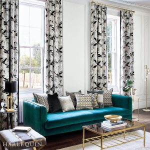 A room with wooden flooring and a blue-green nordic sofa with many pillows, a sliding glass window with a flower-designed extra long curtains installed by Katandra Interiors Busselton.