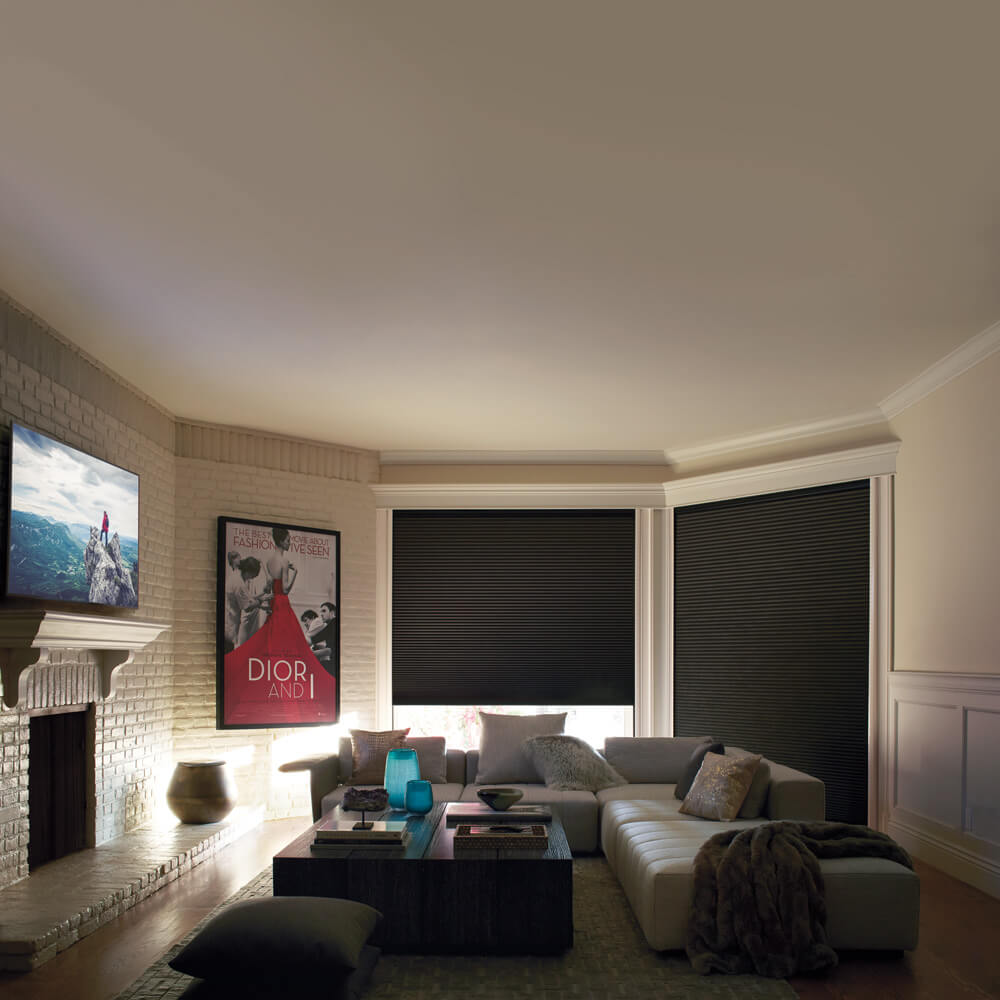 A living room with wooden flooring and a white & gray sofa with many pillows, 2 windows with a black blinds assembled by Katandra Interiors Busselton.